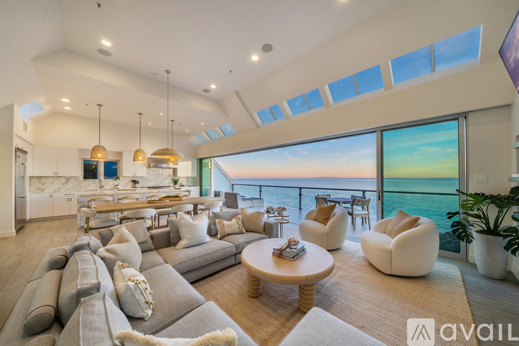 A modern living room with a large grey sofa and a glass wall overlooking the sea.