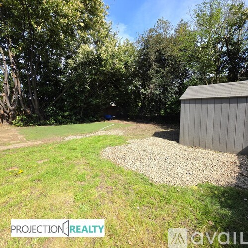 A gravel area in front of a shed with trees in the background.
