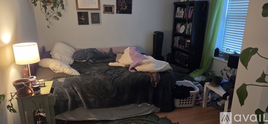 A messy bedroom with a bed in the center and a bookshelf to the right.