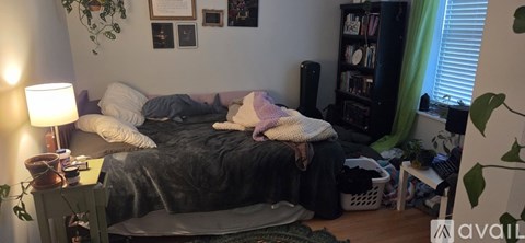A messy bedroom with a bed in the center and a bookshelf to the right.