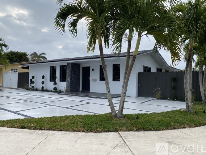 A white building with black windows and doors is surrounded by palm trees.