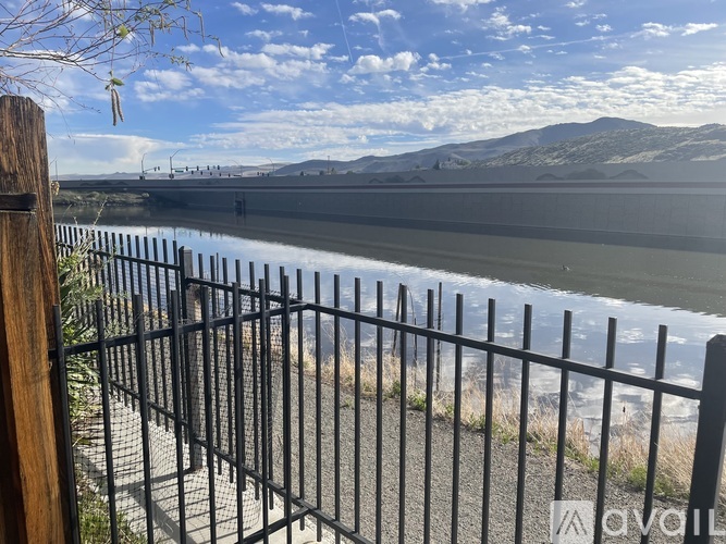 A black fence with a wooden post in front of a body of water with mountains in the background.