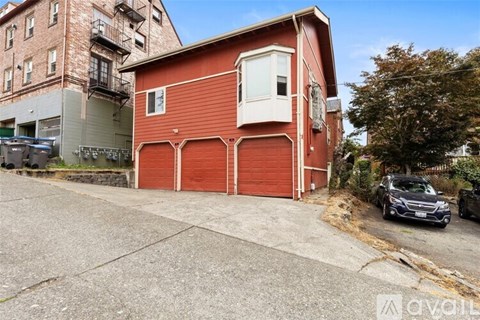 A red building with a white door and windows is situated in front of a grey building.