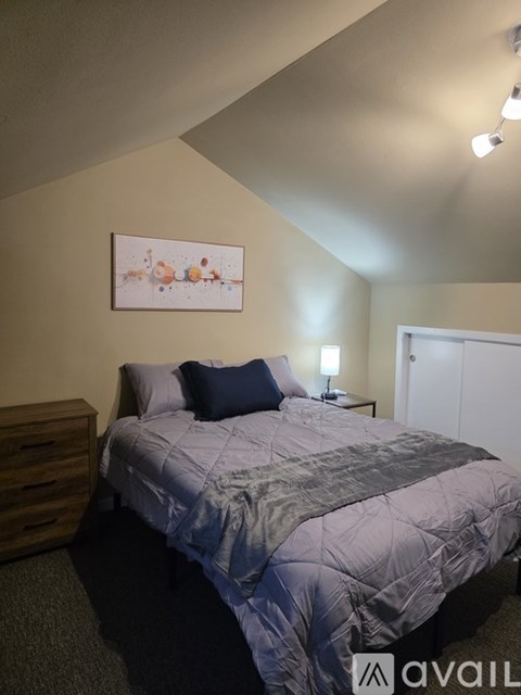 A bedroom with a bed, nightstand, and a painting on the wall.