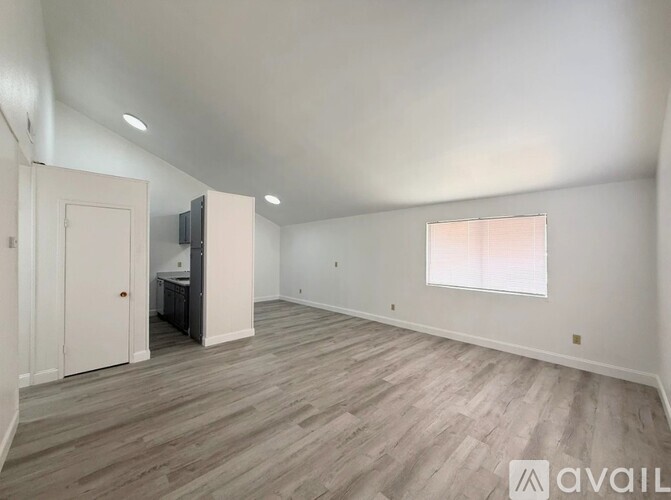A spacious room with wood flooring and a window with blinds.