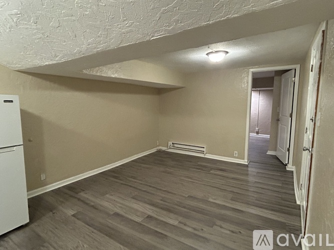 A room with wooden flooring and a white refrigerator.