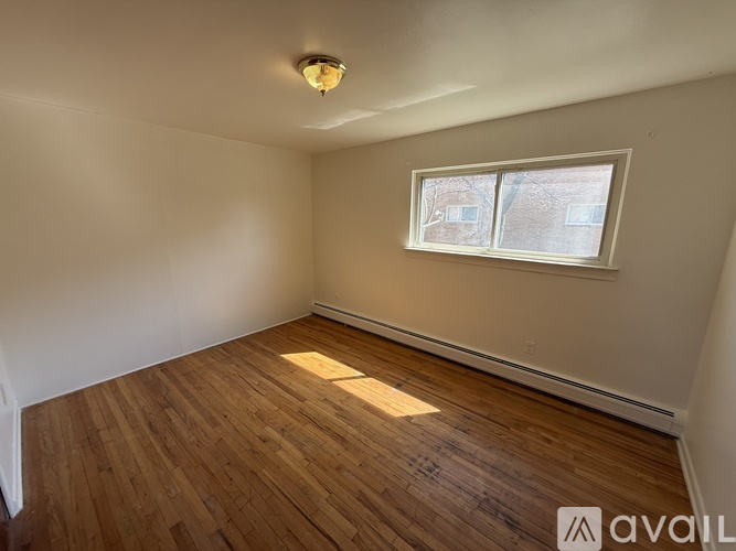 A room with wooden flooring and a window letting in sunlight.