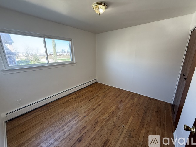 A room with wooden flooring and a window overlooking a field.