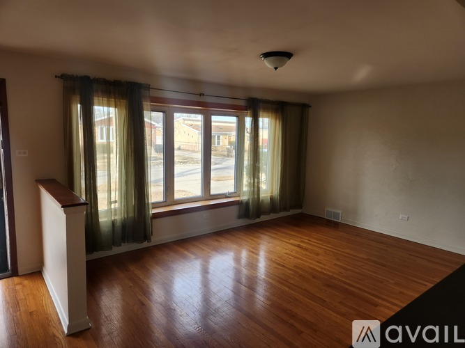 A room with wooden floors and a large window with curtains.