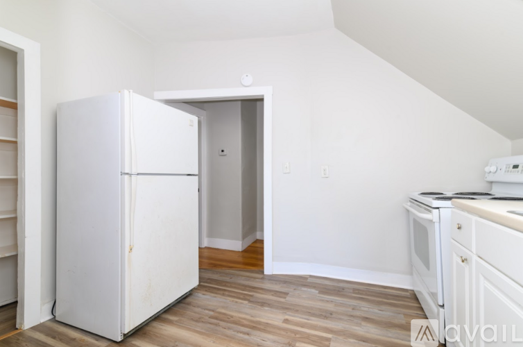 A white refrigerator is in a kitchen with a wooden floor.