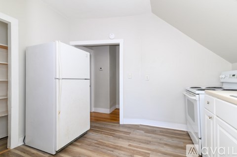 A white refrigerator is in a kitchen with a wooden floor.