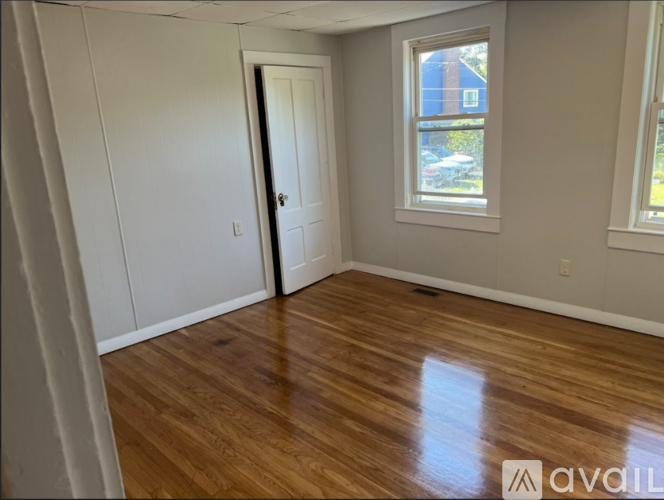 A room with wooden flooring and a window showing a blue building outside.