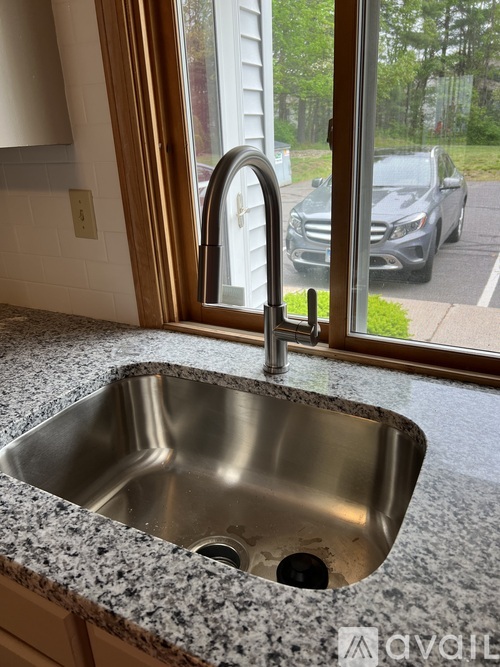 A kitchen sink with a granite countertop and a window overlooking a street.