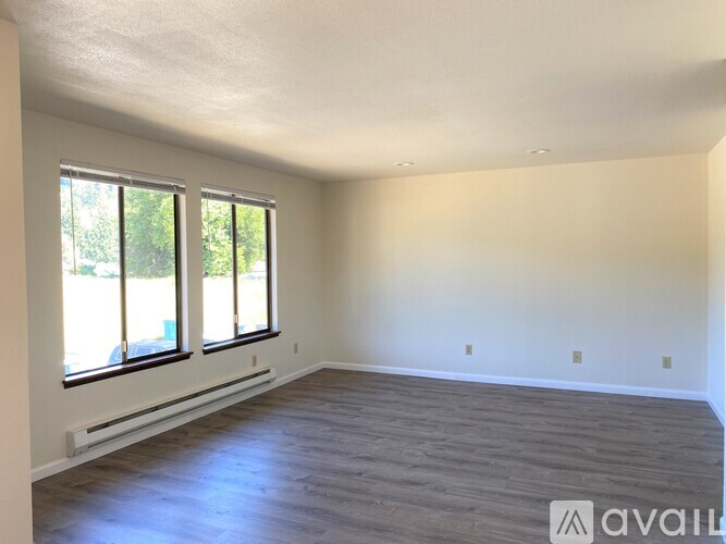 A spacious room with wooden flooring and large windows.