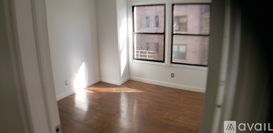 A room with wooden floors and a window showing a building outside.