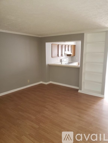 A room with wooden flooring and a window showing a kitchen.