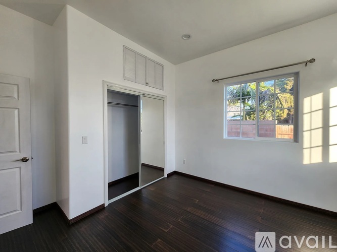 A room with a white door, a window with a view of trees, and a wooden floor.