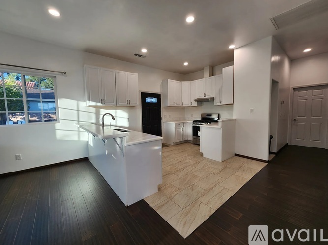 A modern kitchen with white cabinets and a wooden floor.