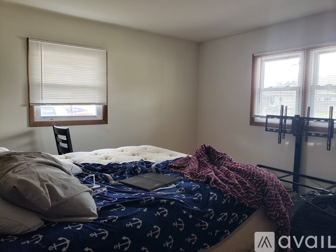 A bedroom with a bed covered in a blue and white bedsheet with anchor designs on it.