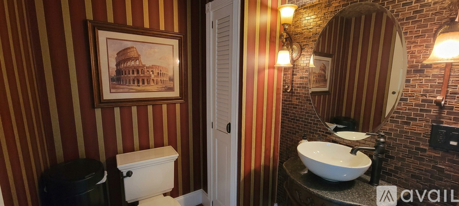 A bathroom with a toilet, sink and a painting of a building on the wall.