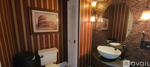 A bathroom with a toilet, sink and a painting of a building on the wall.