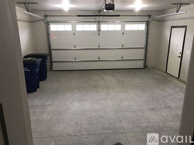 A spacious garage with a white door and a blue trash bin.