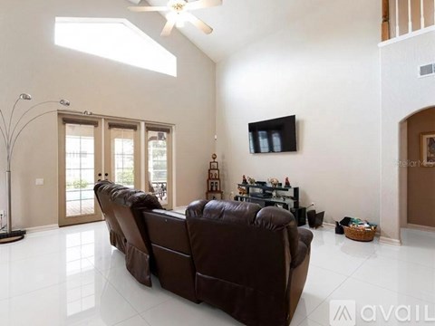 A living room with a brown leather couch and a flat screen TV mounted on the wall.