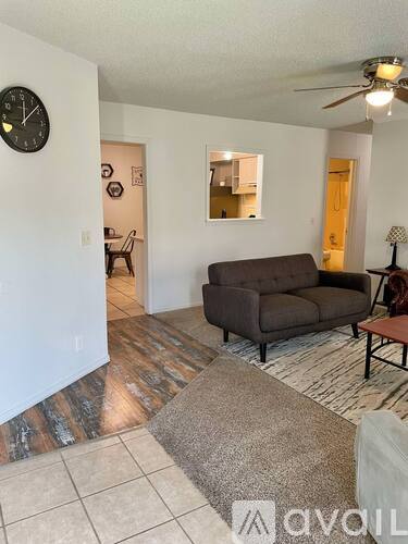 A living room with a couch, a chair, a rug, and a clock on the wall.