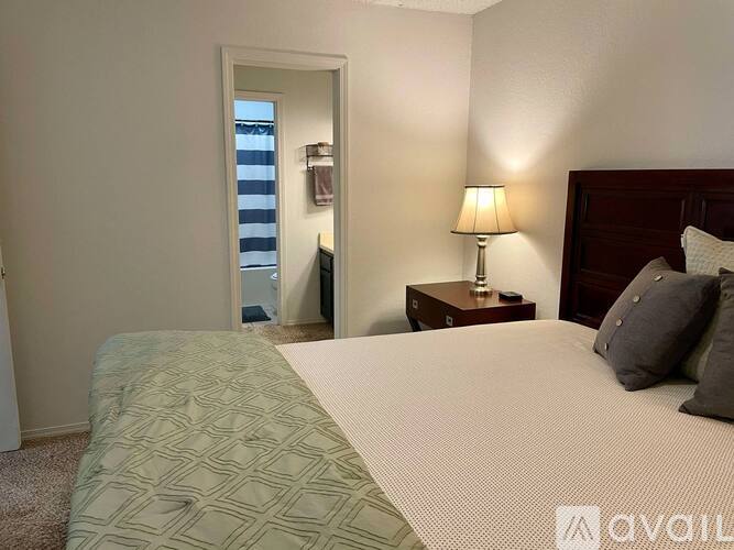A bedroom with a large bed, a nightstand with a lamp, and a door leading to a balcony.