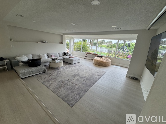 A spacious living room with a grey rug and a large window overlooking a garden.