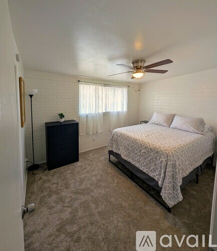 A bedroom with a bed, a ceiling fan, and a window with curtains.