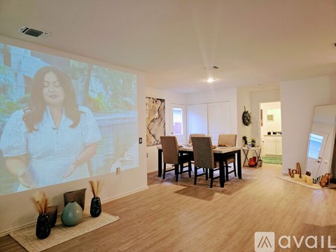 A living room with a dining table and chairs, a large screen on the wall, and a rug with pinecones and a green ball on it.