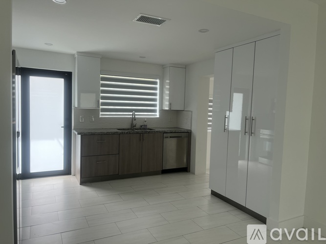 A modern kitchen with a sink, cabinets, and a window with blinds.