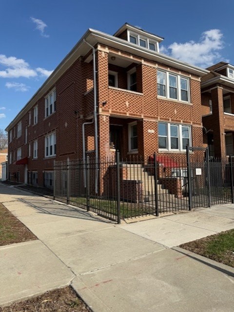 A red brick apartment building with a black fence in front.