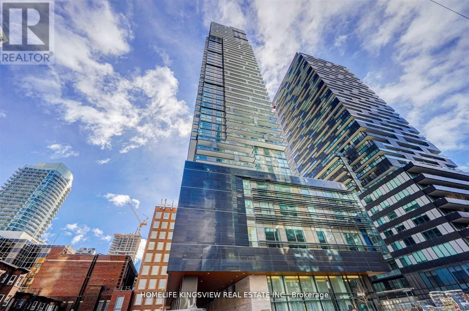 A tall building with a glass facade stands in front of other buildings.