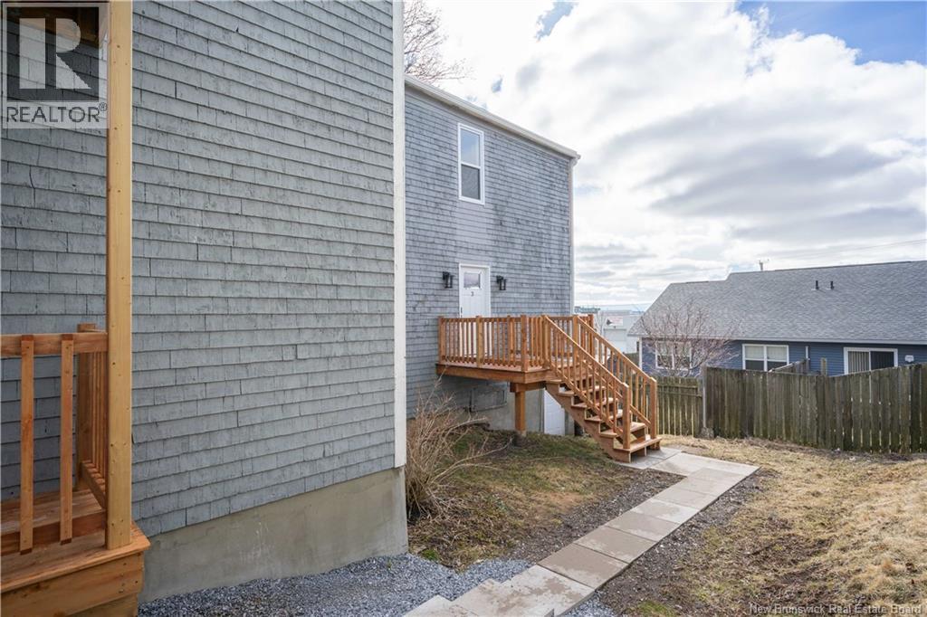 A grey house with a wooden deck and stairs leading to a grey building.