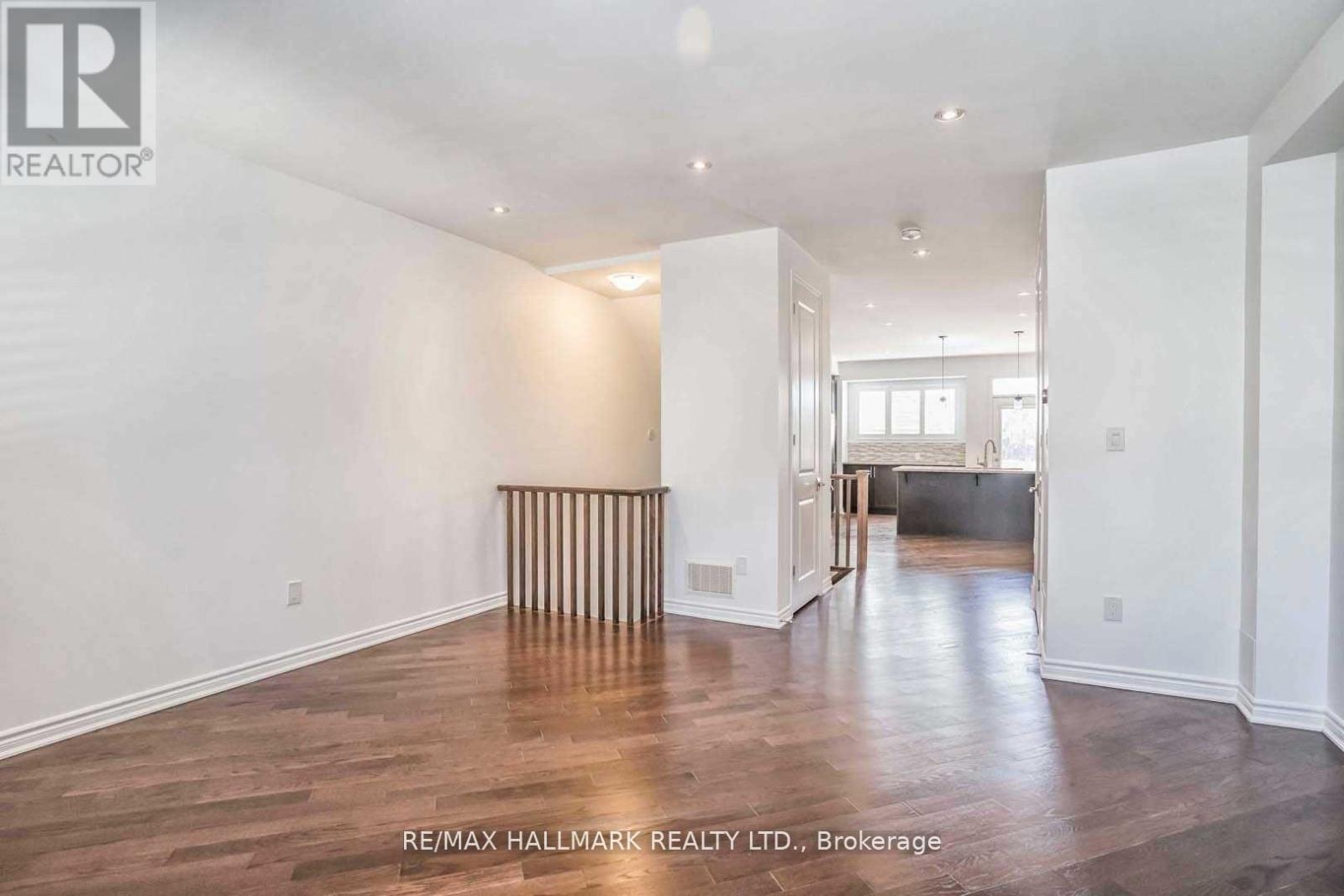 A spacious room with wooden flooring and white walls, with a large window and a door leading to another room.