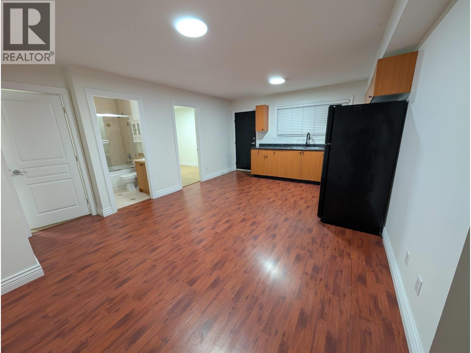 A room with wooden floors and a black refrigerator.