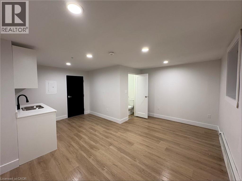 A room with wooden flooring and white walls, with a sink and cabinet on the left side.