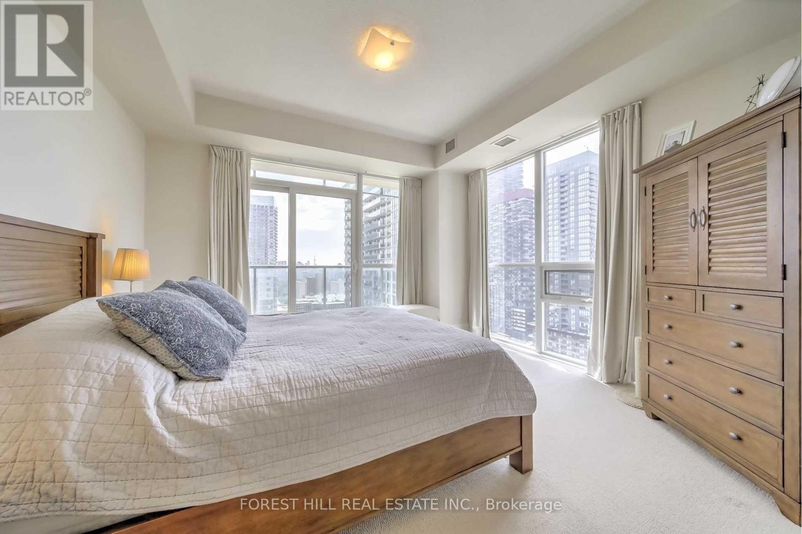 A bedroom with a large bed, a dresser, and a window overlooking a cityscape.