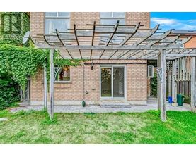 A patio with a pergola and a brick building in the background.