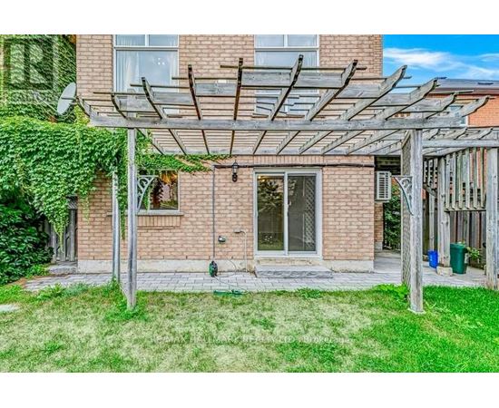 A patio with a pergola and a brick building in the background.