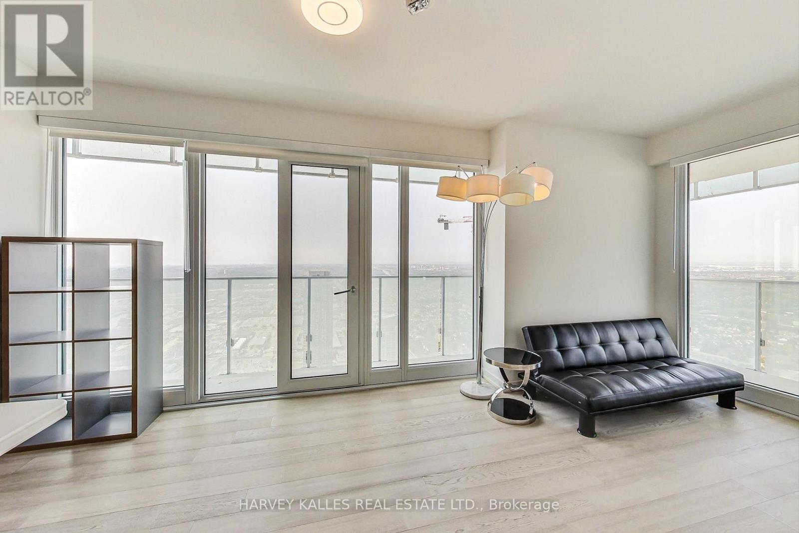A living room with a black leather sofa and a glass door leading to a balcony.