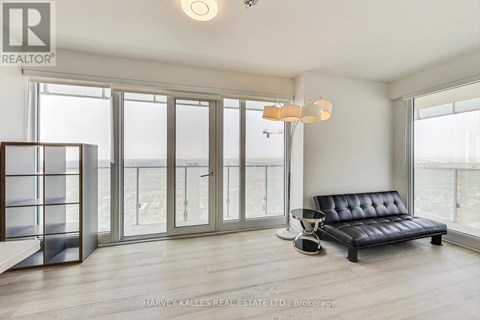 A living room with a black leather sofa and a glass door leading to a balcony.
