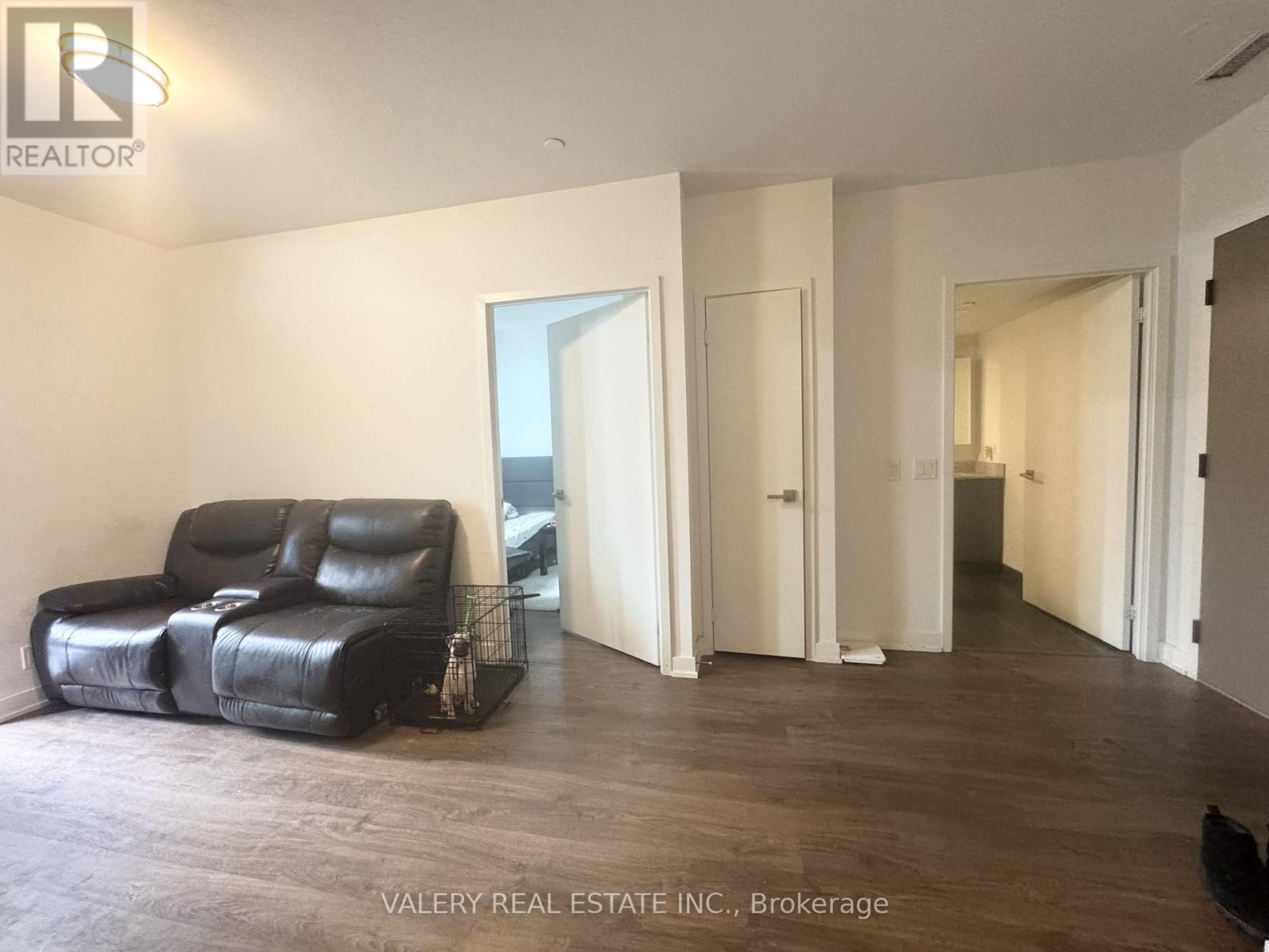 A black leather sofa sits in a spacious living room with white walls and wood flooring.