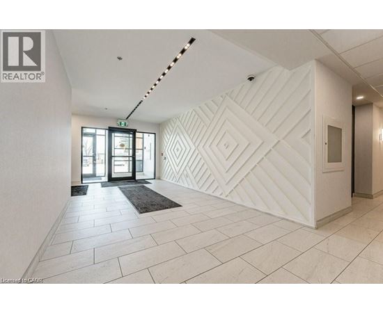 A hallway with a white wall and a black and white rug.