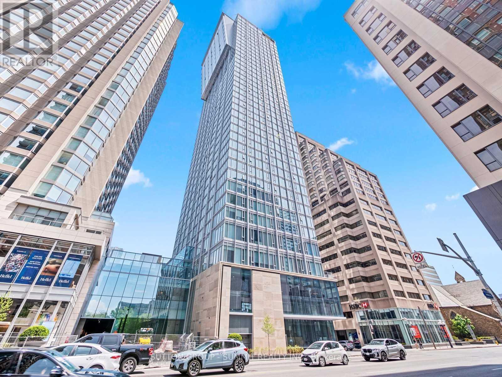 A tall glass building stands in the middle of a street with cars parked in front.