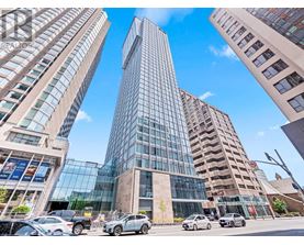 A tall glass building stands in the middle of a street with cars parked in front.