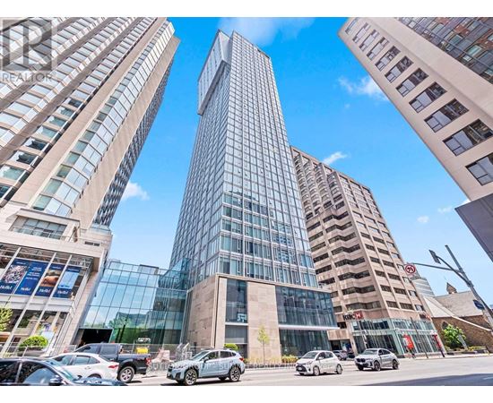 A tall glass building stands in the middle of a street with cars parked in front.