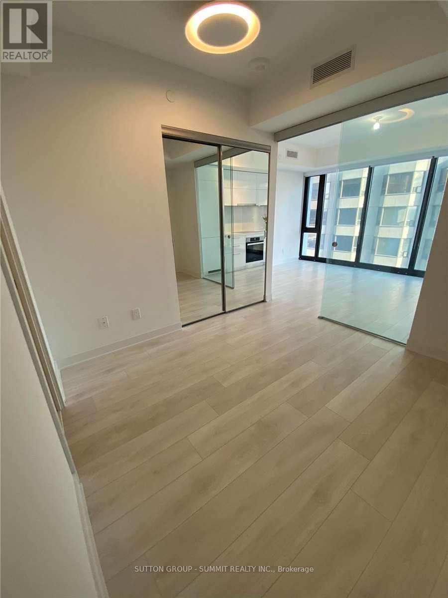 A spacious room with wooden flooring and a glass door leading to a balcony.